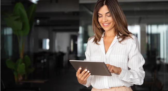 Smiling woman in a white blouse looking at a tablet in an office