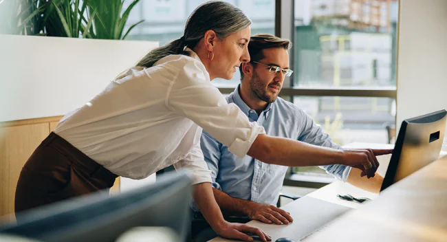 Two colleagues working together at a computer in an office setting