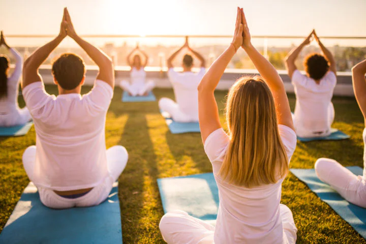 Back view of group of relaxed people exercising Yoga with their arms raised on a terrace.